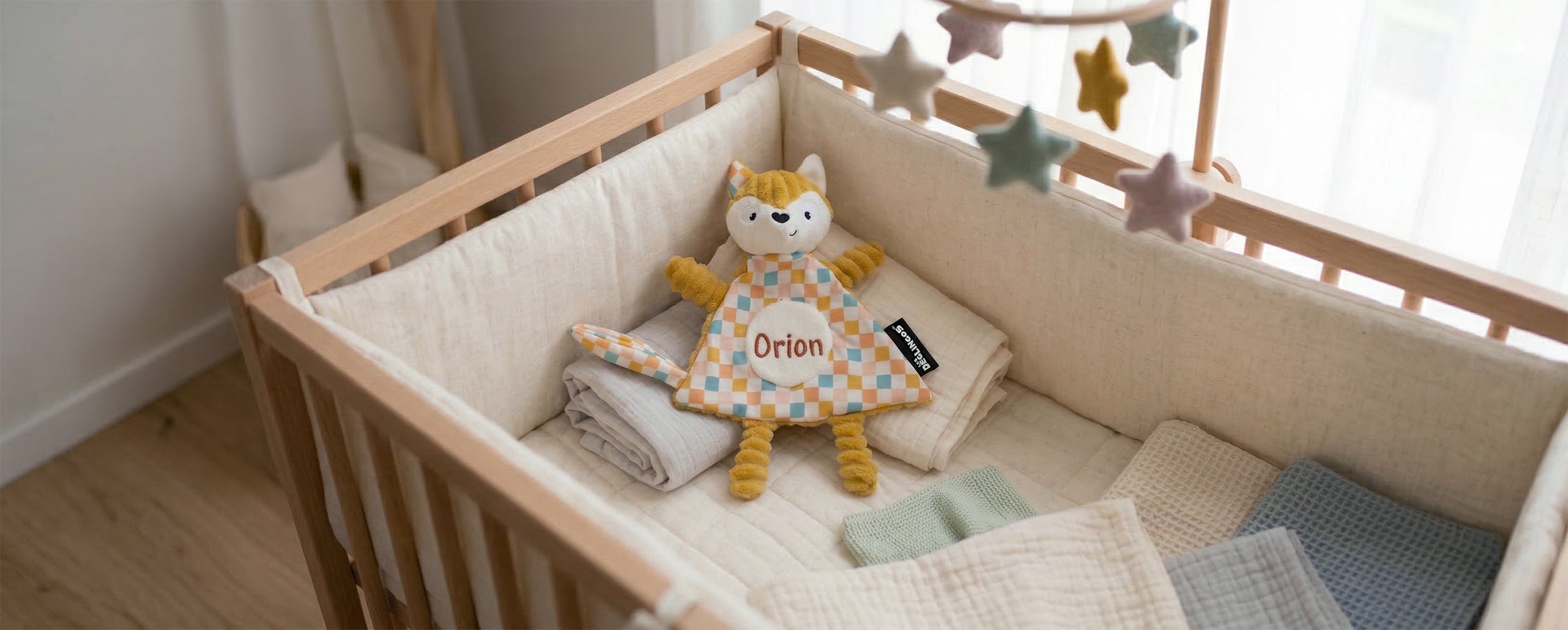 Collection broderie - Visuel d'ambiance d'un doudou Cyranos le renard brodé et installé dans un lit bébé - Les Déglingos